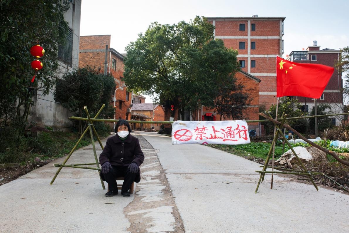 郎村讓老人家守在通往鎮上的三個入口。一位居民坐在其中一處入口，該處用中國國旗和一塊寫著「禁止通行」的布告擋住路。PHOTOGRAPH BY ROBAN WANG, NATIONAL GEOGRAPHIC