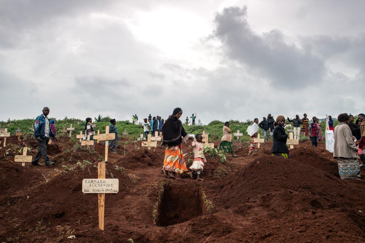 2019年3月2日，厚厚雲層之下，成群結隊的哀悼者在新墳之間慢慢行走，當時他們正走去參加DRC布滕博的基塔圖巴墓園裡50歲員警塔布．阿姆利．艾曼紐（Tabu Amuli Emmanuel）的葬禮。這處墓園坐落於山丘上，可俯瞰布滕博這座DRC東北部最大的城市。在剛果與伊波拉病毒的最新戰役中，罹難者就於此處安息。PHOTOGRAPH BY NICHOLE SOBECKI