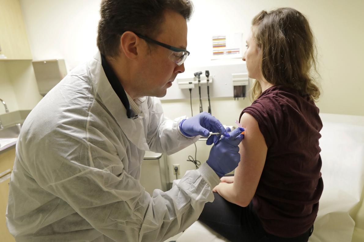 2020年3月16日，藥師麥克．威特（Michael Witte）（左）在一種COVID-19潛在疫苗的臨床試驗第一階段為瑞貝卡．希路爾（Rebecca Sirull）注射疫苗。希路爾是西雅圖凱薩醫療機構華盛頓衛生研究所的研究中第三位接受疫苗的患者，這項試驗的第一階段有三處機構參與，該研究所是其中之一。PHOTOGRAPH BY TED S. WARREN, AP PHOTO 