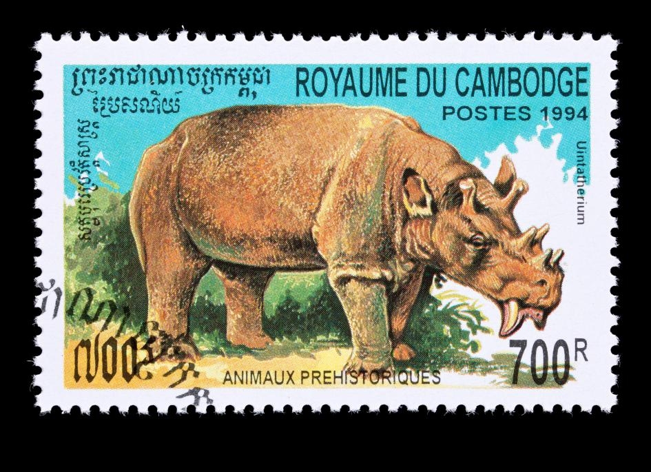 這張柬埔寨郵票上描繪著已滅絕的哺乳動物猶因他獸（Uintatherium），這種5600萬年前的動物神似有著六根粗短的角與長長利齒的犀牛。PHOTOGRAPH BY DBI STUDIO, ALAMY STOCK PHOTO  