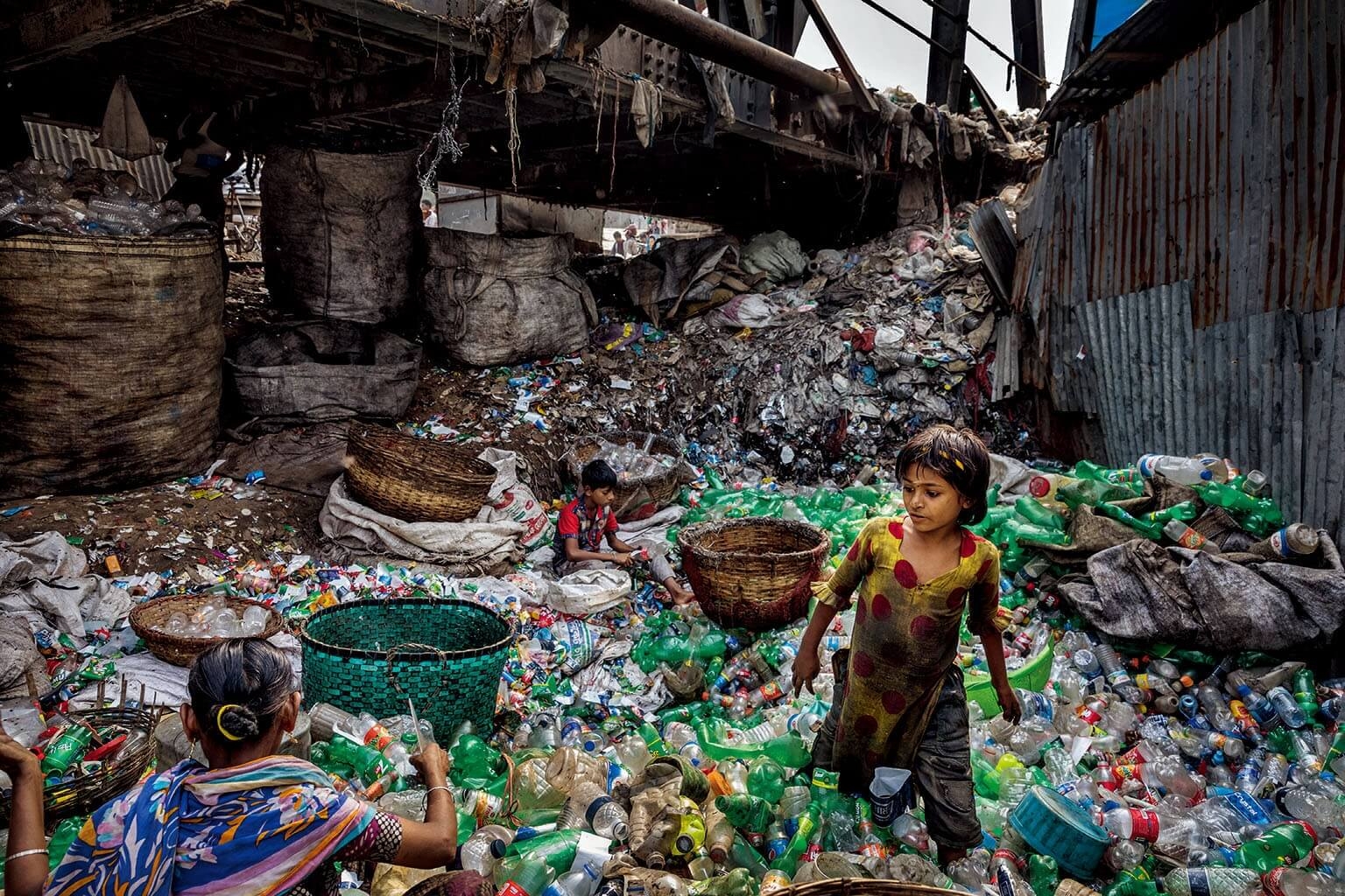 在孟加拉布里甘加河支流的橋底下，一戶人家正在移除塑膠瓶標籤，並分開不同顏色的瓶子。這裡的拾荒者平均一個月可以賺大約100美元。攝影：藍迪．奧森 RANDY OLSON