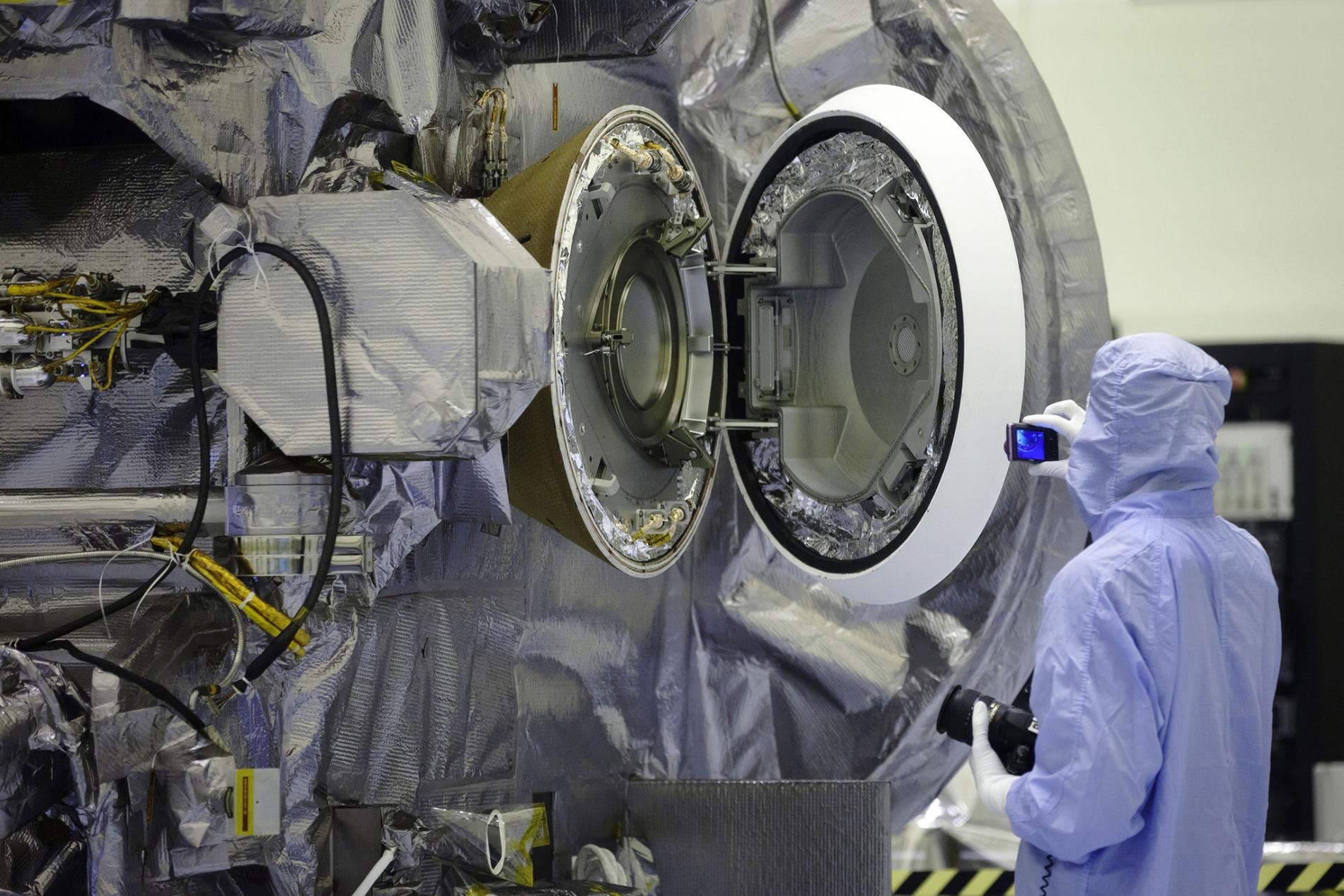 甘迺迪太空中心（Kennedy Space Center）的技術人員在2016年測試艙門時，將門打開檢查樣品返回艙（影像右側圓形物體）的內部。洩漏樣本的採樣頭被放置在這個艙室中，以返回地球。PHOTOGRAPH BY KIM SHIFLETT, NASA 
