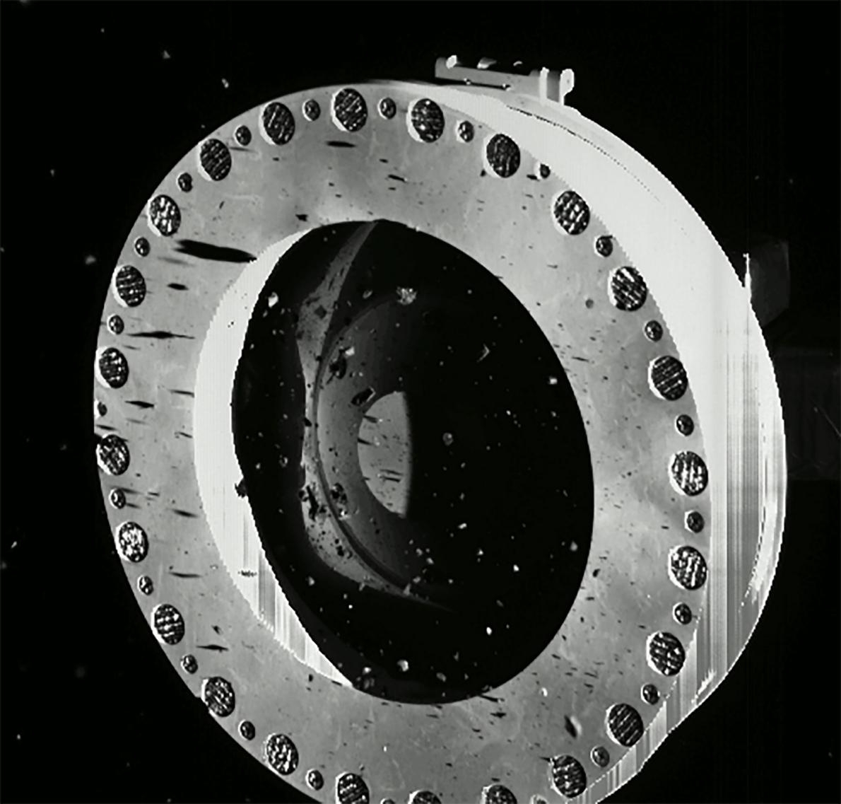 10月22日，在著陸貝努的兩天後，工程師發現歐西里斯號的一觸即走樣本採集裝置採樣頭正在洩漏寶貴的岩石和灰塵。罪魁禍首是因為較大的石塊卡住原本應該要將樣本擋在採樣頭內的聚酯膠膜擋板。PHOTOGRAPH BY NASA/GODDARD/UNIVERSITY OF ARIZONA