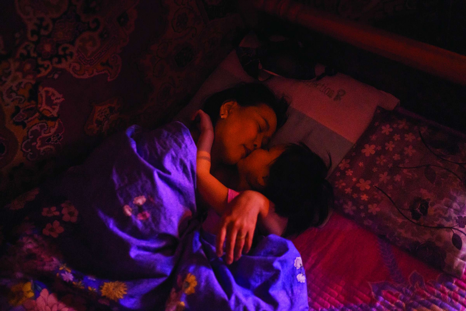 蒙古 在烏蘭巴托，阿坦珠．蘇克邱倫和她的女兒胡蘭在睡前依偎在一起。阿坦珠是她那一區一間家庭診所的護士，在蒙古空汙最嚴重的社區照顧當地婦女和孩童。提姆．海瑟林頓信託贊助了本篇報導的攝影工作。攝影：漢娜．雷耶斯．莫拉雷斯 Hannah Reyes Morales