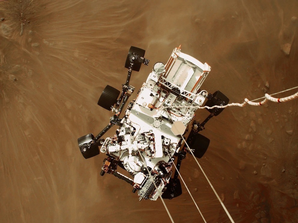 利用「空中吊車」協助探測車著陸──機載相機拍攝了毅力號探測車成功登陸火星的影像和影片，此時的探測車以電纜與空中吊車相連，再數公尺就要輕觸火星地表。PHOTO FROM VIDEO BY NASA/JPL/CALTECH
