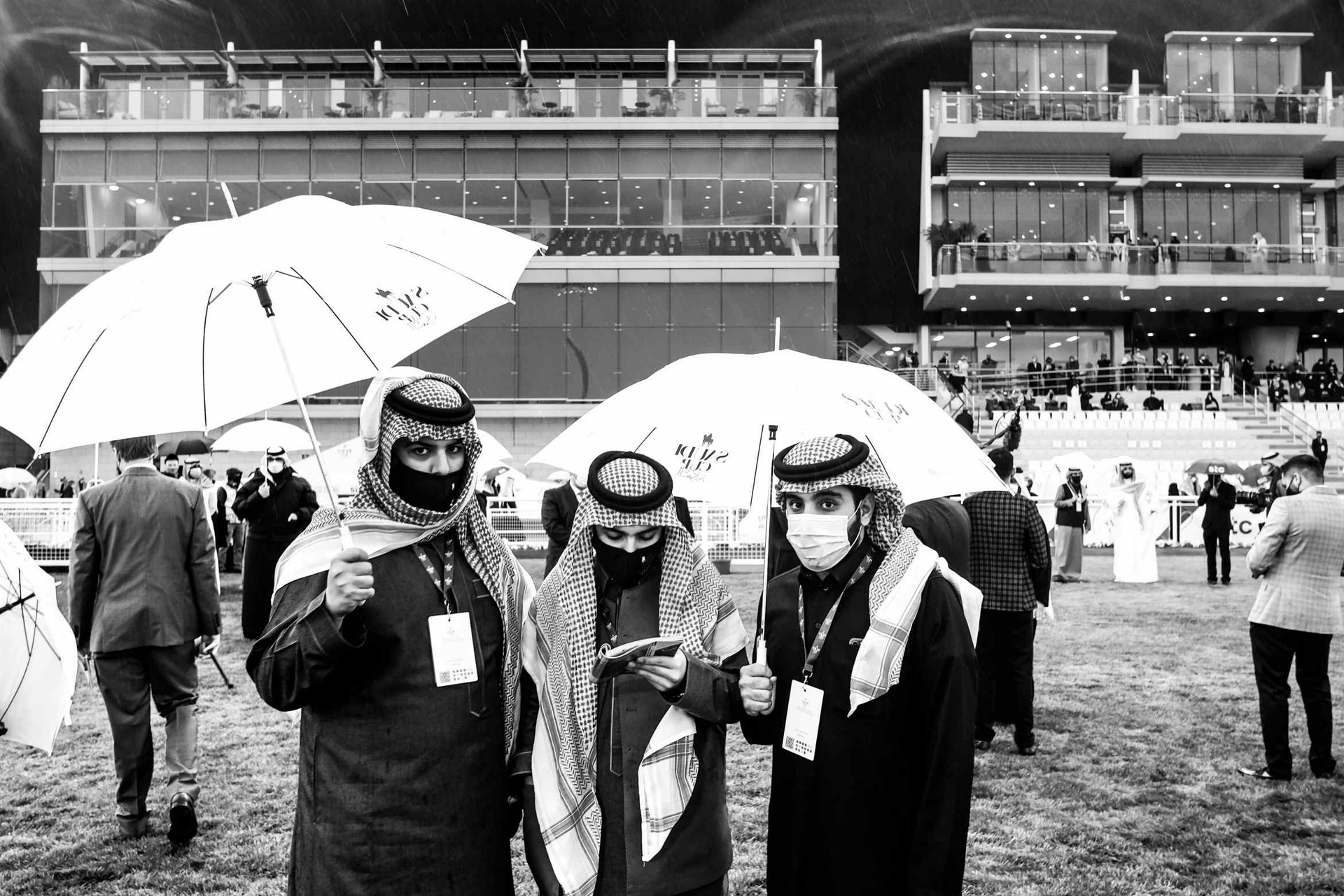 <b>2021 年沙烏地杯 –</b> 在一場不尋常的降雨中，三名面戴口罩的年輕賽馬粉絲在沙烏地杯會議期間，進到阿卜杜勒阿齊茲國王賽馬場的展示圈中。