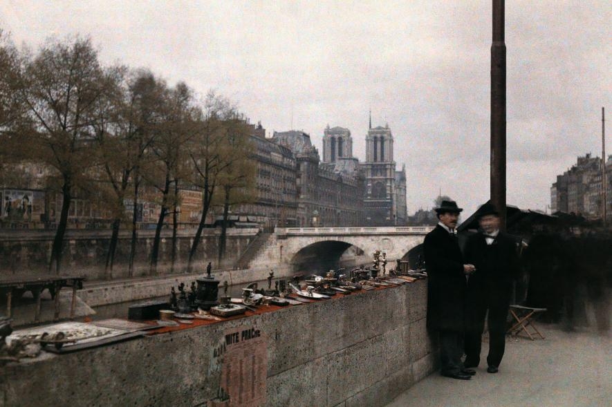 1920年代，兩個男人站在塞納河畔待價而沽的小飾品旁邊，背後就是巴黎聖母院。PHOTOGRAPH BY JULES GERVAIS COURTELLEMONT, NAT GEO IMAGE COLLECTION